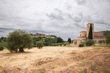 Obraz premium Abbey Sant Antimo (Abbazia di Sant'Antimo), in a lowland among olive trees and cypresses and on a hilltop a town Castelnuovo dell'Abate. Tuscany, Italy