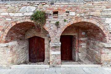 Fototapeta na wymiar Arched entrance with thick medieval walls to a building in the Bagno Vignoni. Tuscany, Italy