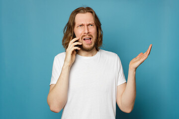 Shocked man talking on mobile phone on blue background