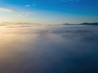 Fototapeta premium The rays of dawn over the fog in the Ukrainian Carpathians. Aerial drone view.
