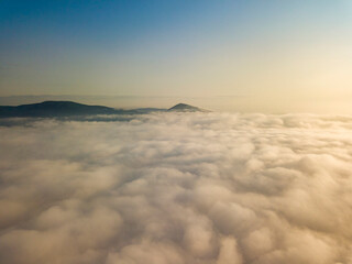Flight over fog in Ukrainian Carpathians in summer. Mountains on the horizon. Aerial drone view.