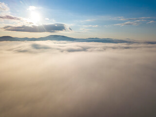 Flight over fog in Ukrainian Carpathians in summer. Mountains on the horizon. A thick layer of fog covers the mountains with a continuous carpet. Aerial drone view.