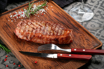 Fried ramp or strip beef steak served with seasonings and herbs on a wooden board. Cooking steak on the grill