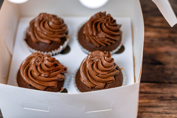 Set of four chocolate mafins in cardboard box. Cupcakes are decorated with chocolate butter cream.