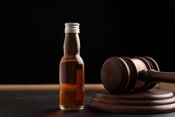 Judge gavel and bottle with whisky or other alcohol on black background. Alcohol and crimes concept.