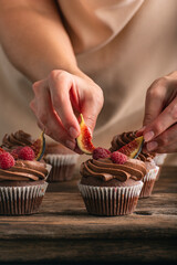 Pastry chef decorates muffin with raspberries and figs. Close up photo of cupcakes preparation....