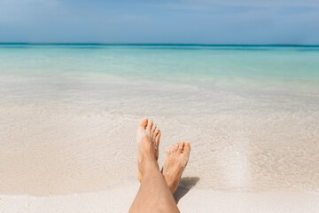 Holiday concept. Woman feet close-up relaxing on beach, enjoying sun and splendid view