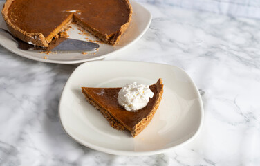 homemade pumpkin pie on a light background and a slice on a white plate, thanksgiving dessert