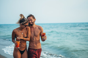 Attractive young couple with alcohol cocktails walking on the beach