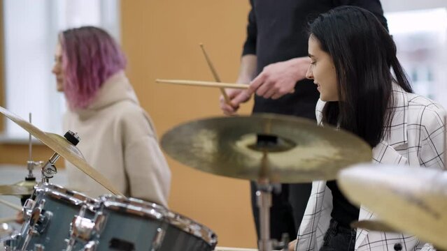 Young adult men and women learn to play drums at school. Hobbies and pastime. Art and life style.