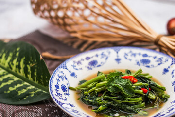 Stir Fried Morning Glory with Soybean Paste Served in a Chinese-patterned dish with spotted leaves, onions, shallots on the table.