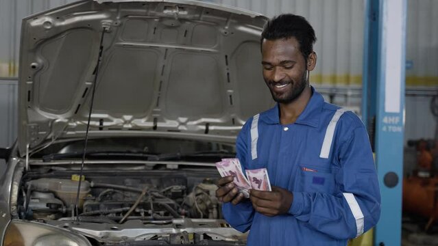 Mechanic in front of car at garage couting Indian currency notes - concept of repair or maintenance business profits, earnings and banking