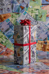 Gift box wrapped in paper with the image of American dollars on the background of paper Kazakhstani tenge