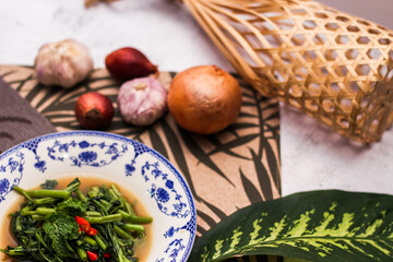 Stir Fried Morning Glory with Soybean Paste Served in a Chinese-patterned dish with spotted leaves, onions, shallots on the table.