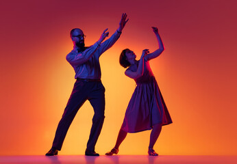 Portrait of excited man and woman, couple of dancers in vintage retro style outfits dancing lindy hop dance isolated on gradient yellow and purple background.
