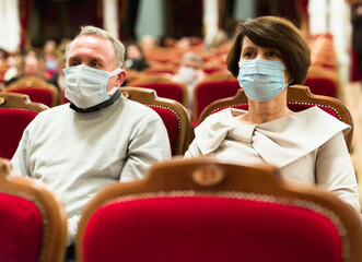 mature man and woman in antivirus mask in theater watching a performance