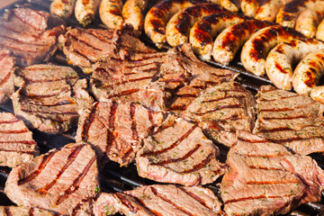 Meat steaks with sausages are grilled close-up.