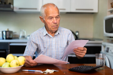 Elderly man sitting in kitchen with utility bills