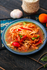 Spicy papaya salad served in a blue dish with sticky rice in a bucket and long beans, dried chilli and vegetables.
