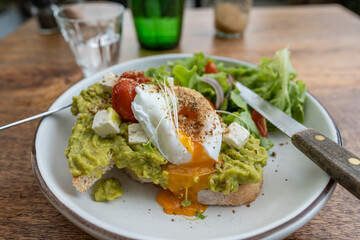 Sourdough toast, poached eggs, avocado pulp and fresh vegetables on plate in cafe, close up