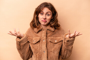Young caucasian woman isolated on beige background doubting and shrugging shoulders in questioning...