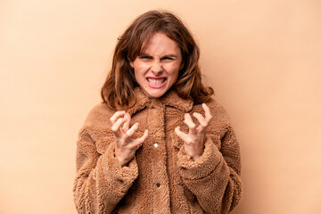 Young caucasian woman isolated on beige background upset screaming with tense hands.