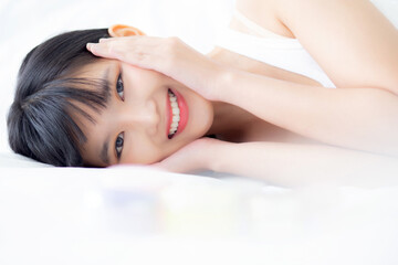 Obraz premium Beautiful of young asian woman smiling and lying on bed at bedroom, beauty of girl touch cheek with hygiene and healthy, cream and lotion, cosmetic and makeup, skin care and lifestyles concepts.