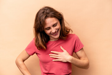 Young caucasian woman isolated on beige background laughing keeping hands on heart, concept of happiness.