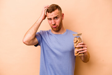 Young caucasian man holding cookies jar isolated on beige background being shocked, she has remembered important meeting.