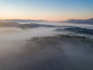 Fototapeta premium Flight over fog in Ukrainian Carpathians in summer. Mountains on the horizon. Aerial drone view.