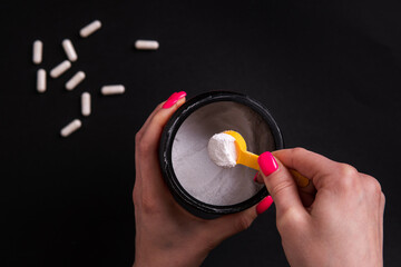Creatine. A woman's hand holds a portion of sports nutrition on a black background close-up.