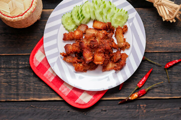 Fried Pork Belly with Fish Sauce and Sticky Rice Served on a white plate on a black wooden floor.