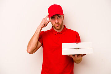 Young delivery caucasian man holding pizzas isolated on white background pointing temple with finger, thinking, focused on a task.