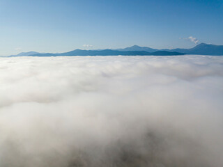 Flight over fog in Ukrainian Carpathians in summer. Mountains on the horizon. A thick layer of fog covers the mountains with a continuous carpet. Aerial drone view.