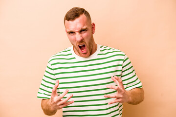 Young caucasian man isolated on beige background upset screaming with tense hands.