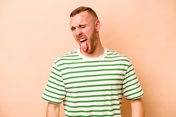 Fototapeta premium Young caucasian man isolated on beige background funny and friendly sticking out tongue.