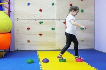 a little girl works on herself and walks with her hands and feet on studded balls in a children's center in white - obrazy, fototapety, plakaty