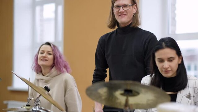 Young adult men and women learn to play drums at school. Hobbies and pastime. Art and life style.