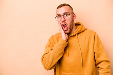 Young caucasian man isolated on beige background shouts loud, keeps eyes opened and hands tense.