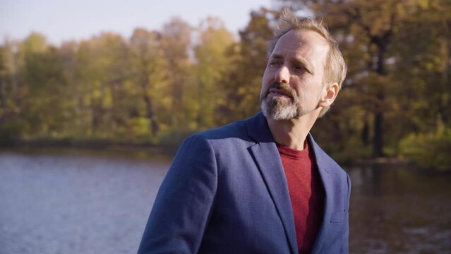A middle-aged handsome Caucasian man thinks about something on a bridge in a park in fall - a river in the background