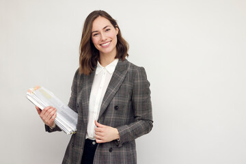 Beautiful and smiling business woman with paperwork in hands, standing isolated on white, looking happy about the papers she's holding and smiling in to the camera.  - 492575348