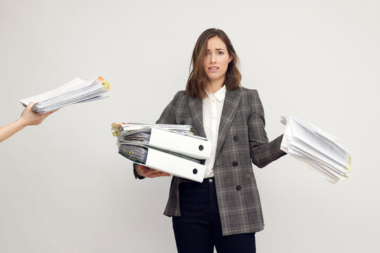 Stressed female worker and business woman holding a pile of paperwork while getting more work to do. Looking frustrated in camera, isolated on white background. Concept: Too much work