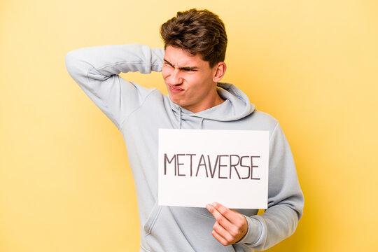 Young caucasian man holding metaverse placard isolated on yellow background touching back of head, thinking and making a choice.