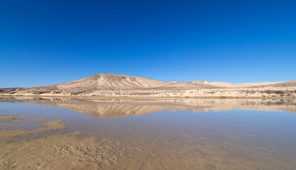 a landscape in sunshine and blue sky. In the background white mountains in the foreground is water, a small lake