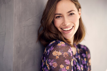 Portrait of young happy woman, looking beautiful with a big smile on her mouth. Posing and looking cute, standing isolated against concrete background in a beautiful dress.