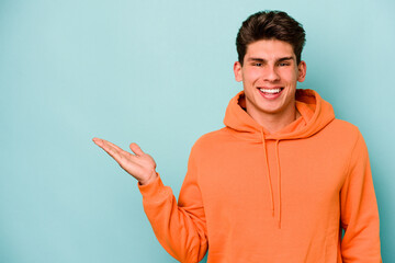 Young caucasian man isolated on blue background showing a copy space on a palm and holding another...