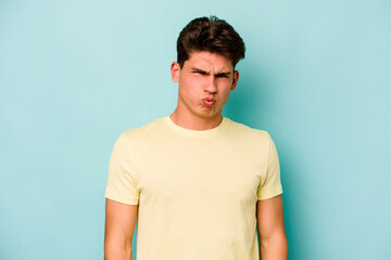 Obraz premium Young caucasian man isolated on blue background blows cheeks, has tired expression. Facial expression concept.