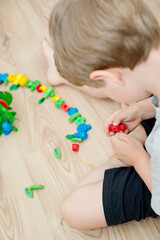 Fine-motoric skils. Stringing Beads Toys for infants and toddlers. Threading Activity for Children. boy sitting on the floor and plays with wooden tree and garden goods.