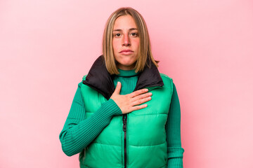 Young caucasian woman isolated on pink background taking an oath, putting hand on chest.