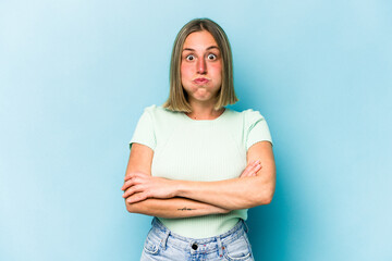 Young caucasian woman isolated on blue background blows cheeks, has tired expression. Facial expression concept.